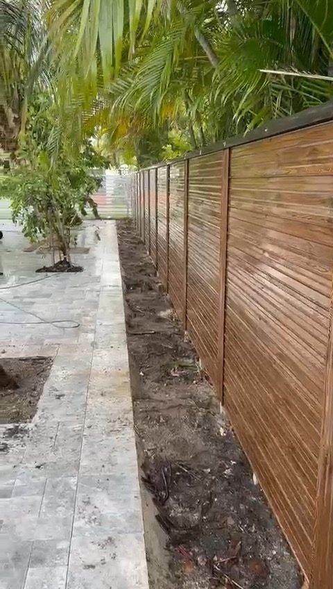 Durafence wood-grain finish along a travertine paver path with palms (powder-coated steel).