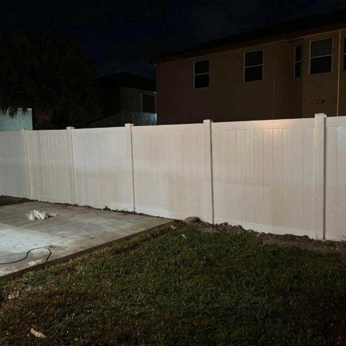 White vinyl privacy fence at night under property lighting.