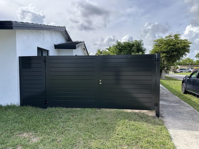 Black horizontal-slat aluminum gate fronting a white South Florida home.