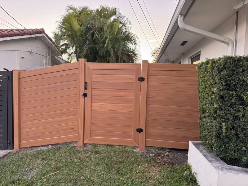 Wood-grain vinyl fence install in South Florida — horizontal panels with a center gate, palm trees at golden hour.